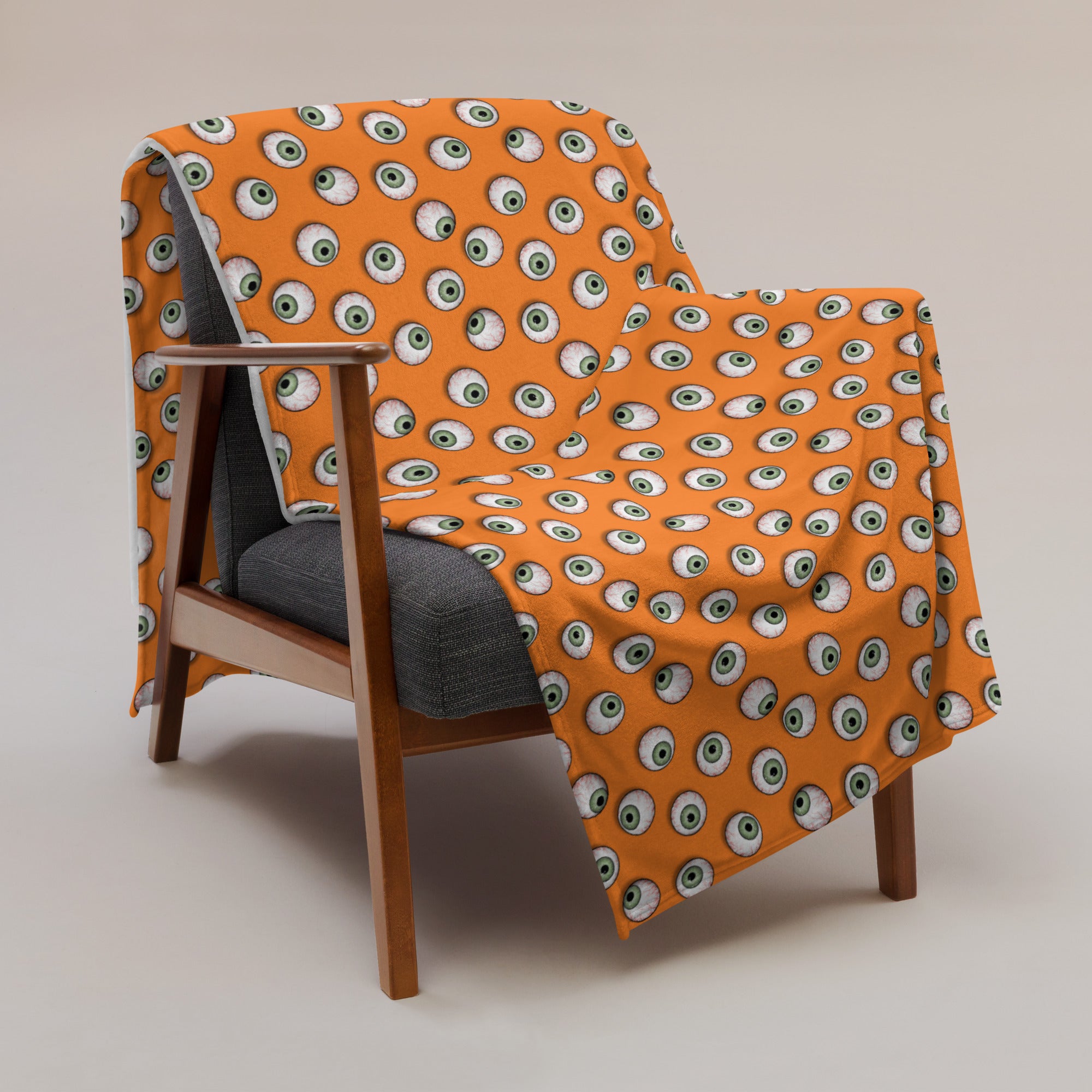 image of 50" x 60" Eye see you blanket draped over a chair with repeated pattern of a eyeballs on an orange background
